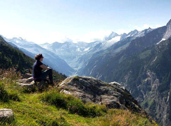 ReSomatic Tirol 2027 Alpesi panoráma Tirolban: hegyoldalon ülő nő a gleccserekkel szegélyezett völgy fölött